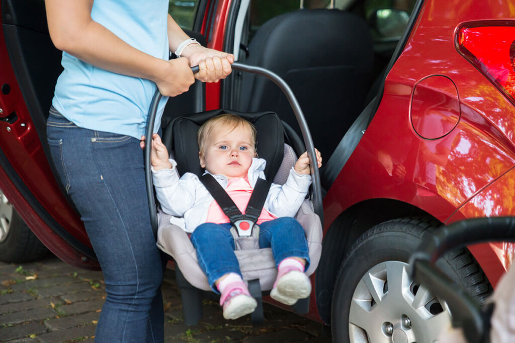 Persona che tiene il marsupio con il bambino davanti a un'auto con la portiera aperta