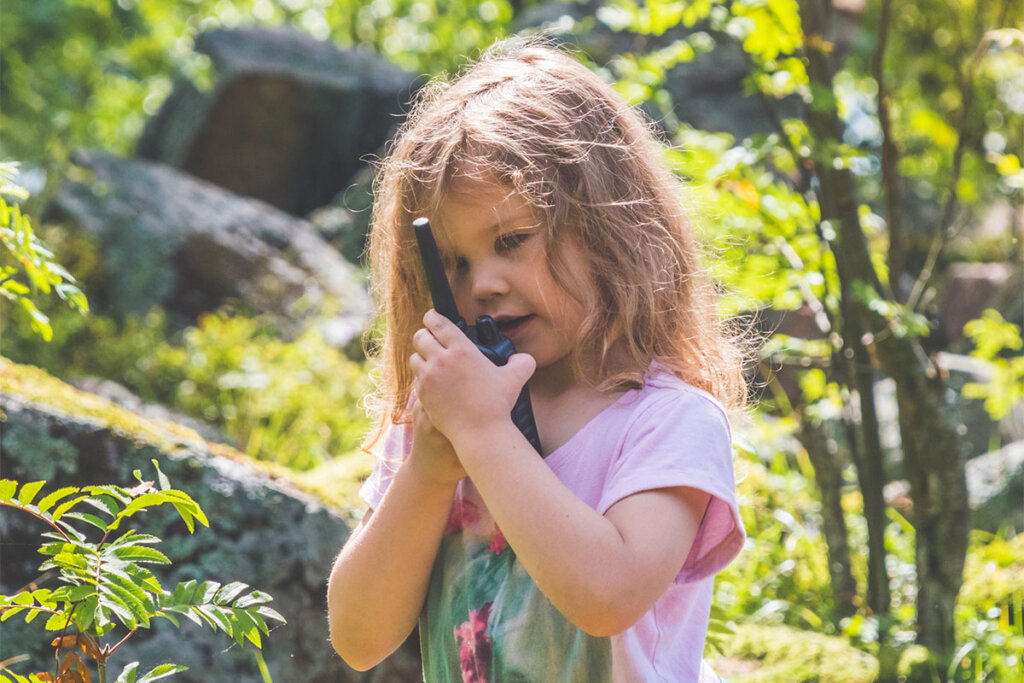 Bambina che parla con un walkie-talkie nella foresta