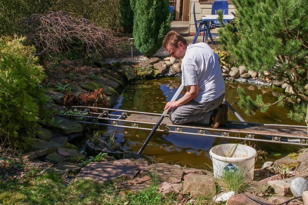 Un uomo pulisce il laghetto da giardino con un aspirapolvere per il fango del laghetto